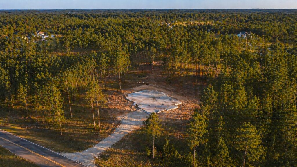 Aerial drone view of a 1-acre wooded rural Walker County lot with a fresh concrete slab foundation poured